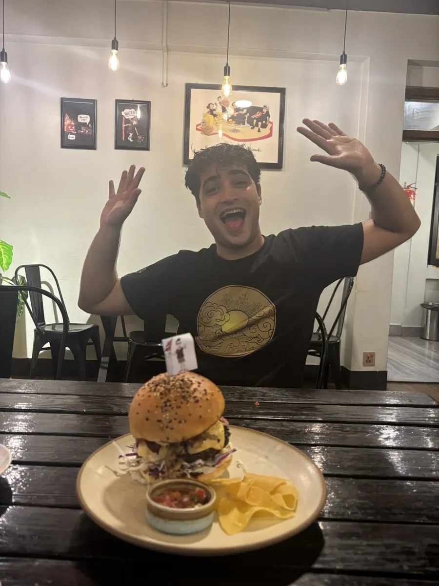 Subash smiling with arms up at a cafe, ready for a meal after the rain